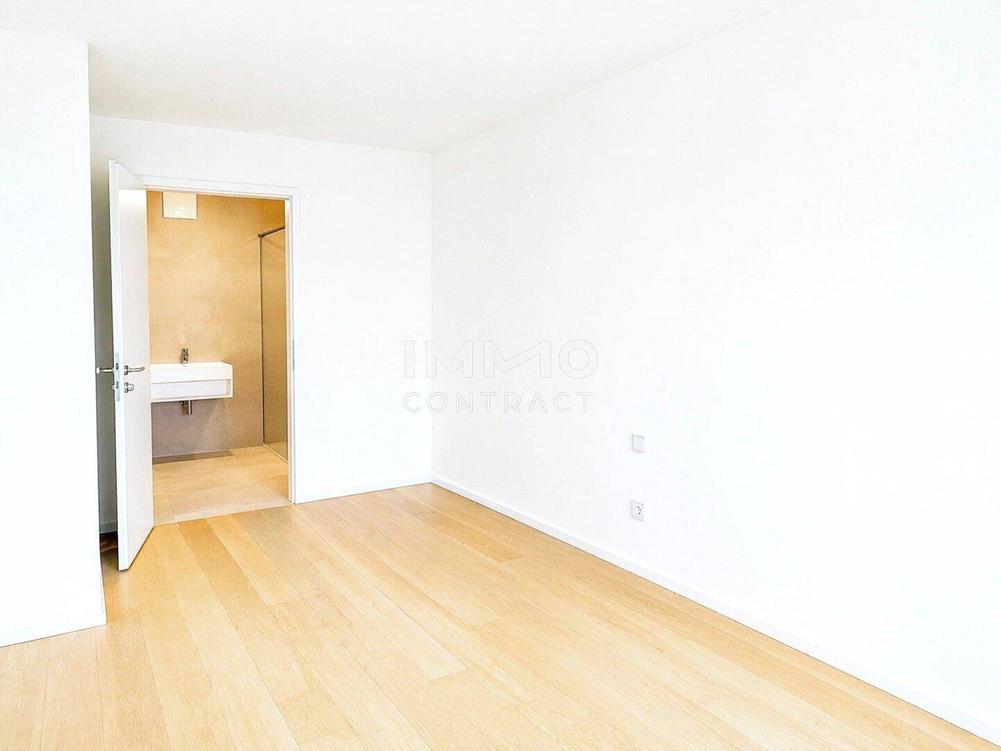 Helles Schlafzimmer mit Parkettboden und direktem Zugang zu einem modernen Badezimmer.