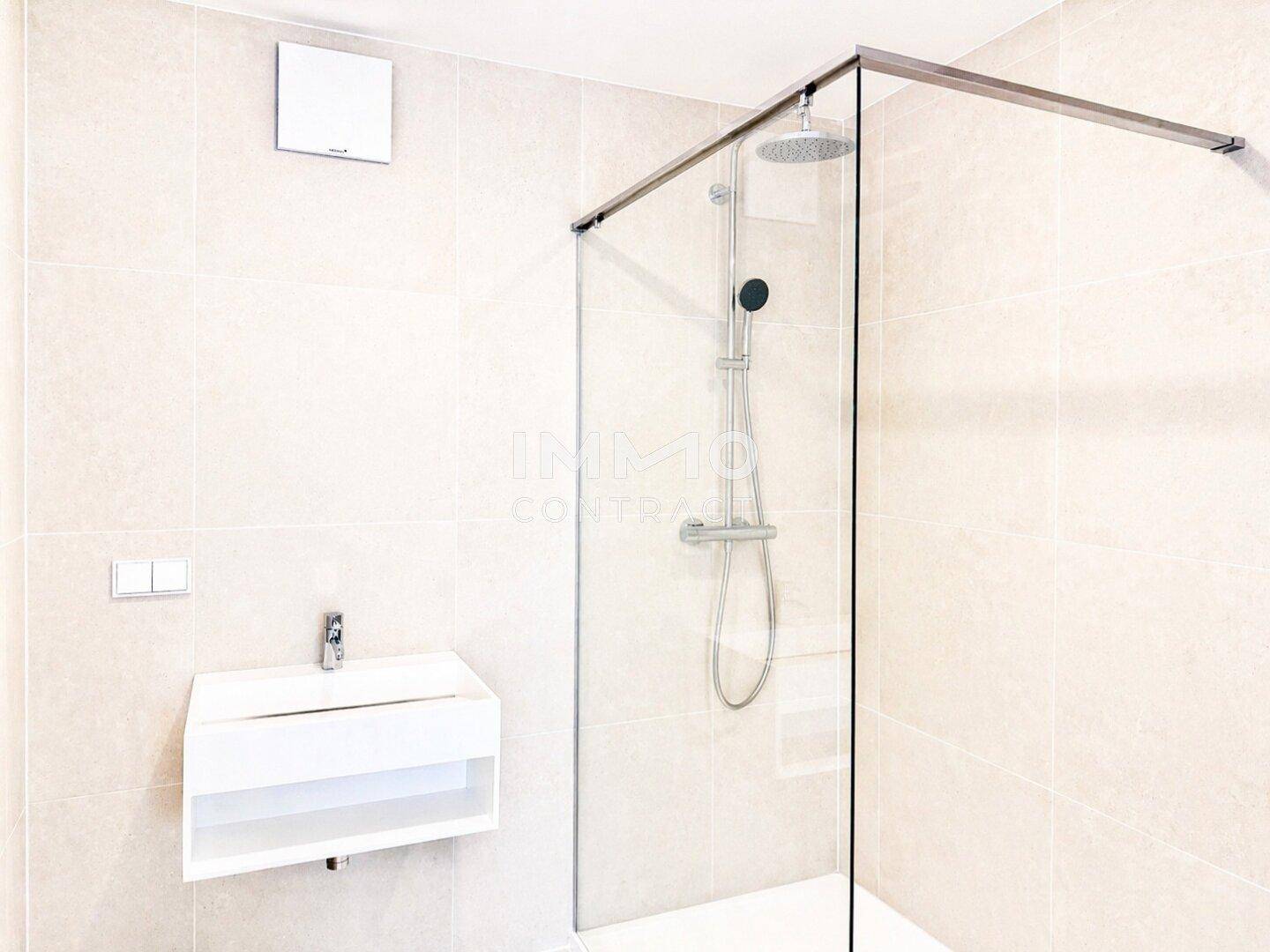 Modernes Badezimmer mit begehbarer Dusche, Wandwaschbecken und hellen Fliesen.