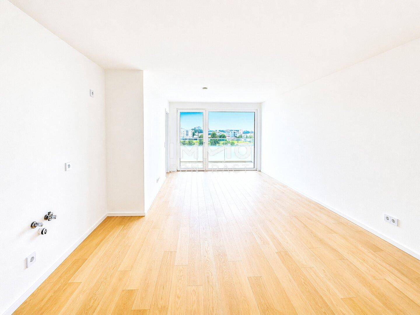 Heller, leerer Raum mit Parkettboden und Zugang zu einem Balkon oder einer Terrasse.