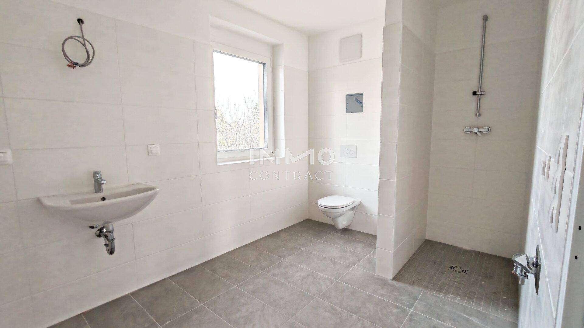 Modernes Badezimmer mit Fliesenboden, Waschbecken, wandhängendem WC und ebenerdiger Dusche.