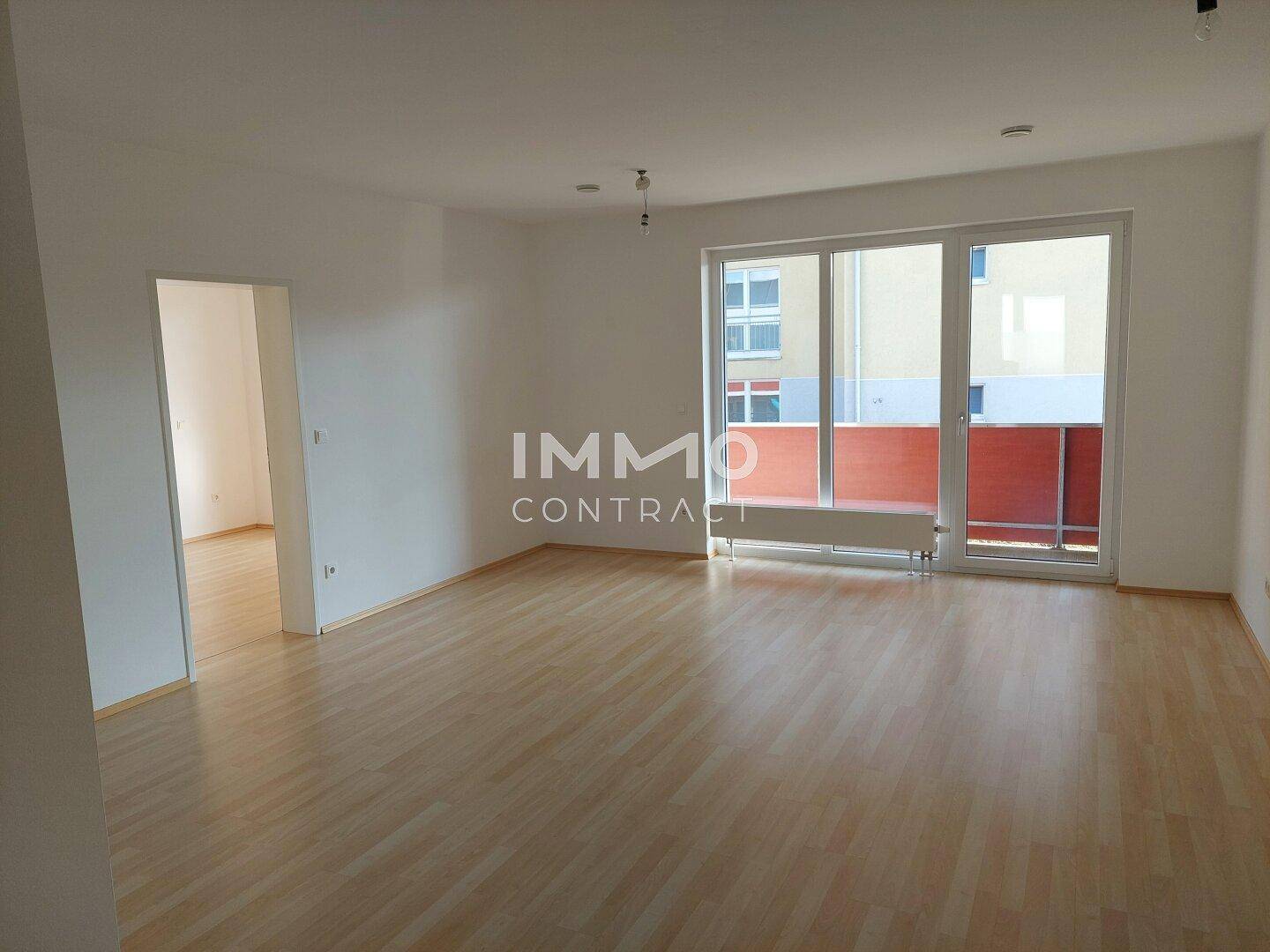 Geräumiger Wohnbereich mit hellem Laminatboden und Zugang zu einem Balkon.