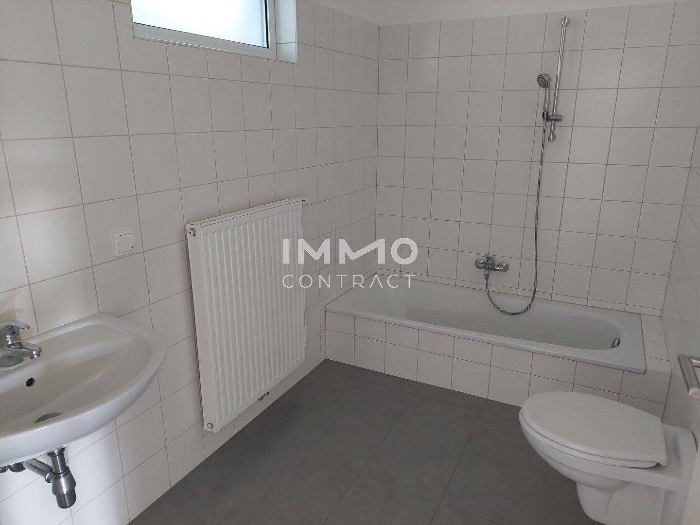 Funktionales Badezimmer mit weißen Fliesen, Badewanne, WC und Waschbecken.