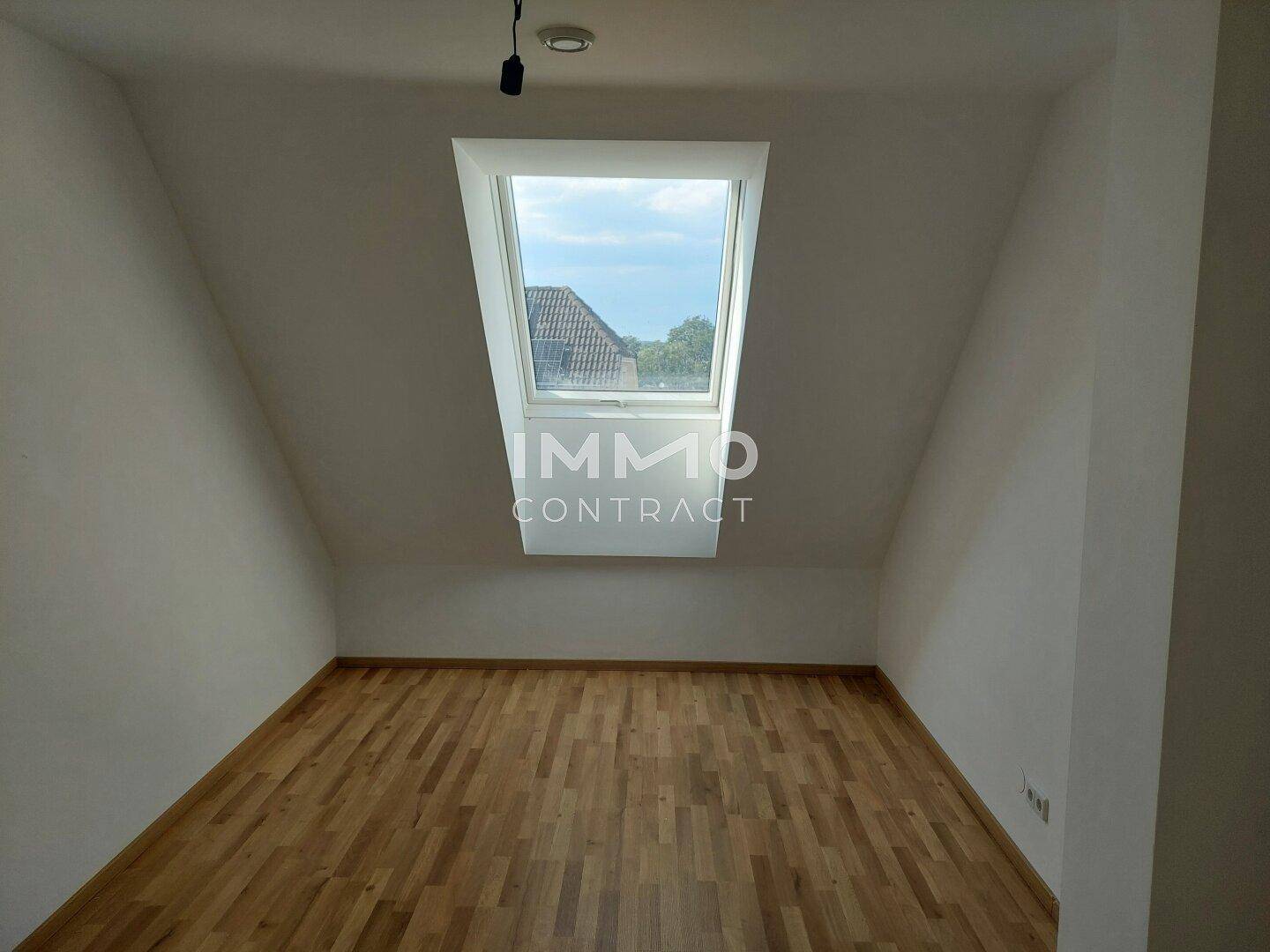 Dachgeschosszimmer mit Parkettboden und einem großen Dachfenster, das viel Licht spendet.