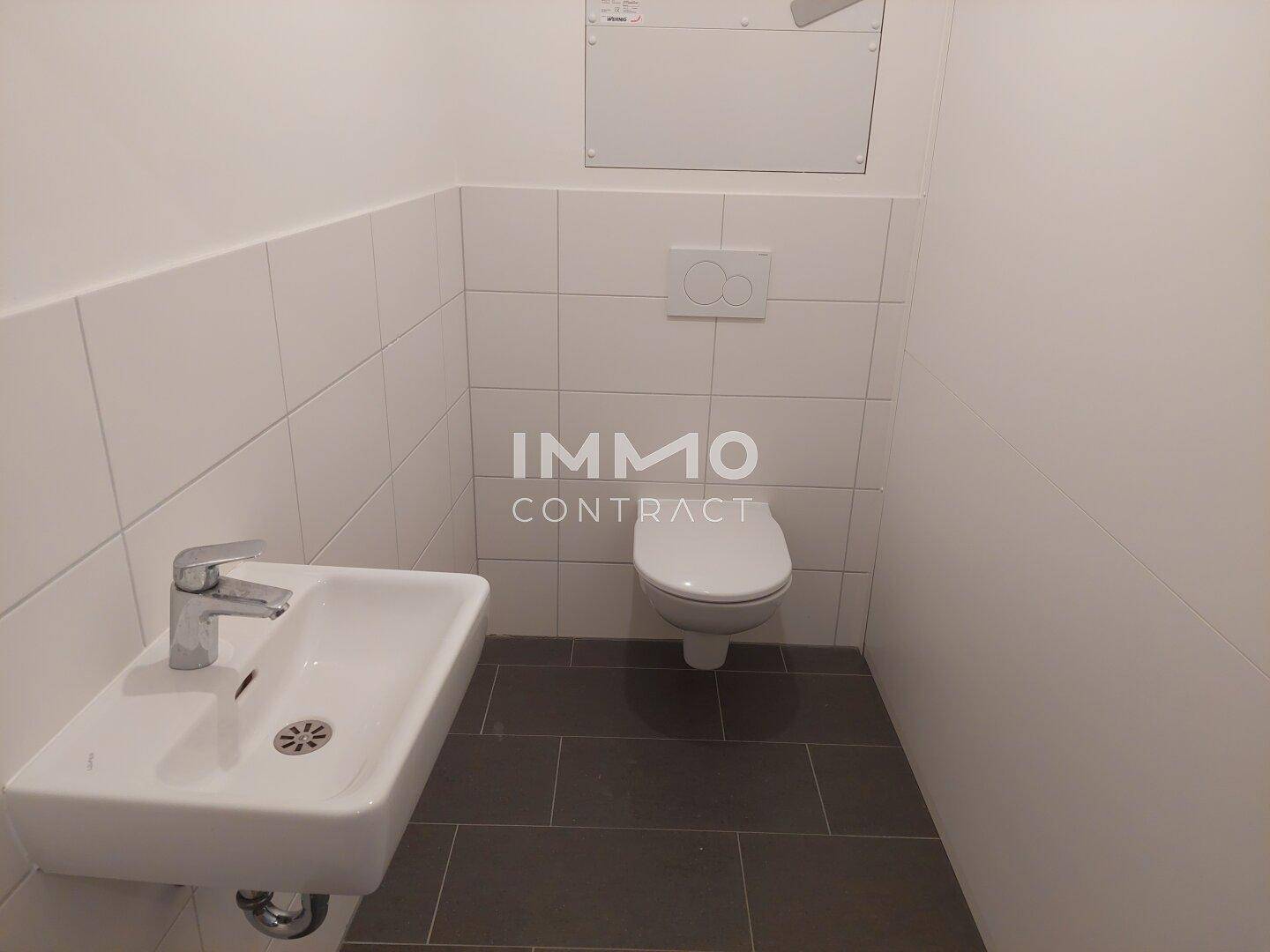 Separates WC mit wandhängender Toilette, kleinem Waschbecken und Fliesenboden.