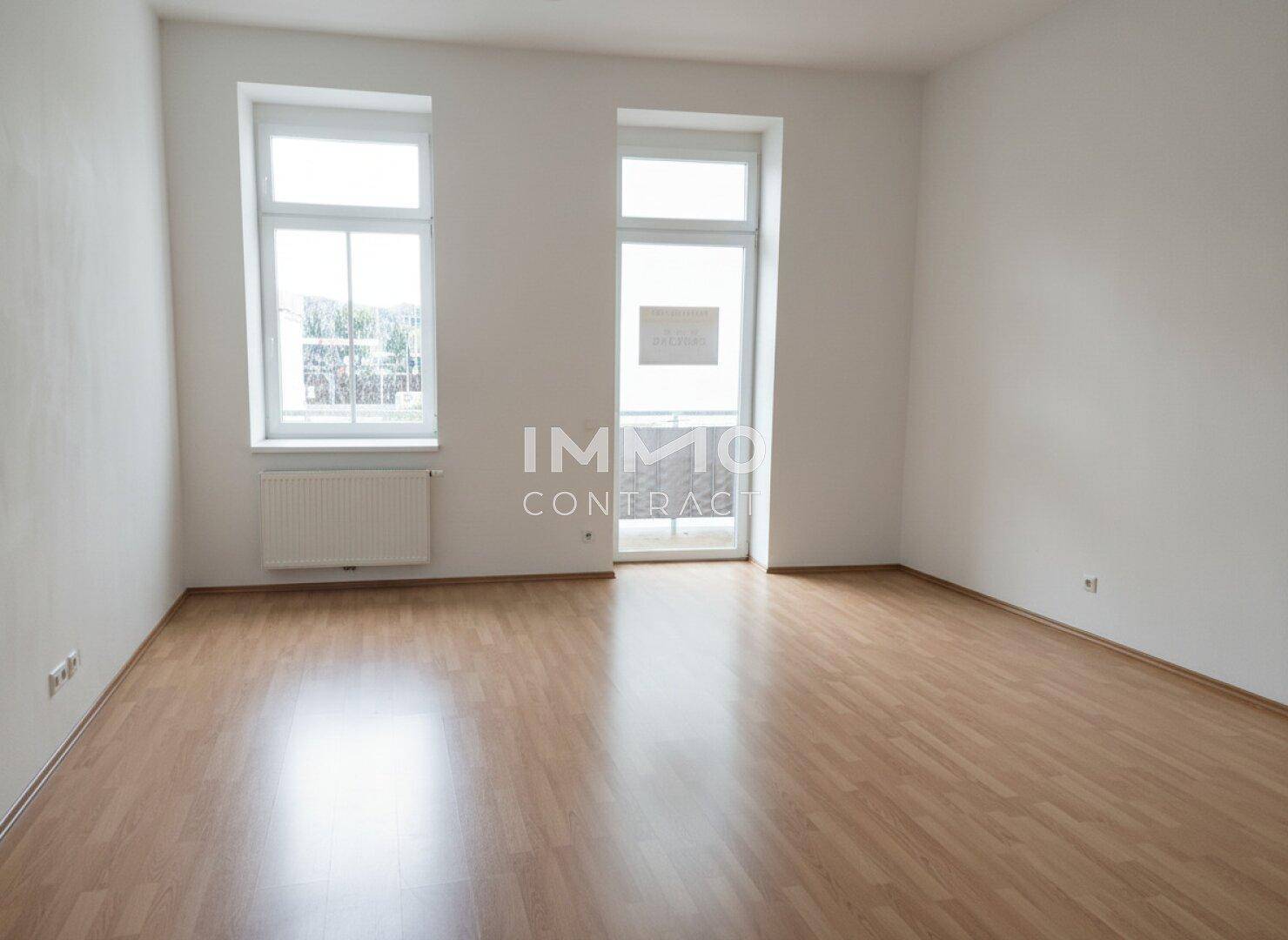 Geräumiger Raum mit Laminatboden und Zugang zu einem französischen Balkon.