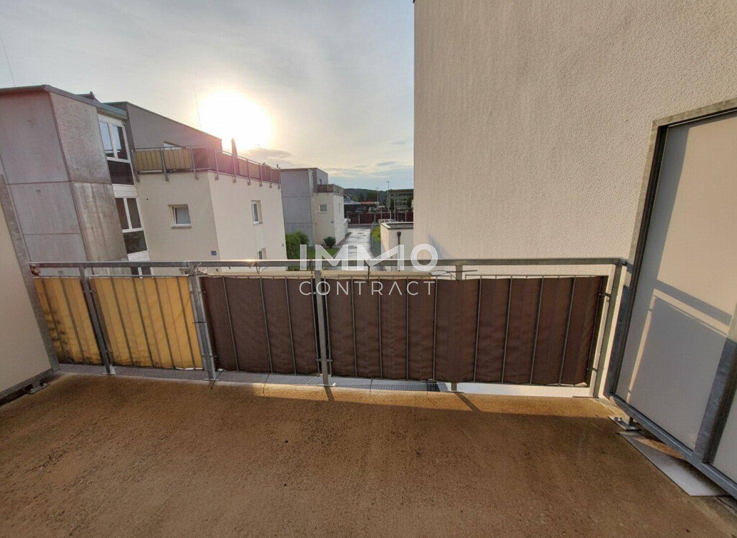 Balkon mit Blick auf die umliegenden Gebäude und den Sonnenuntergang am Horizont.
