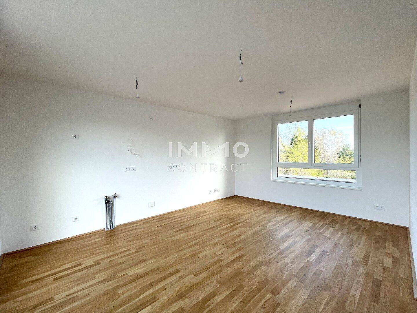 Heller, unmöblierter Raum mit Parkettboden und großem Fenster, das viel Tageslicht hereinlässt.