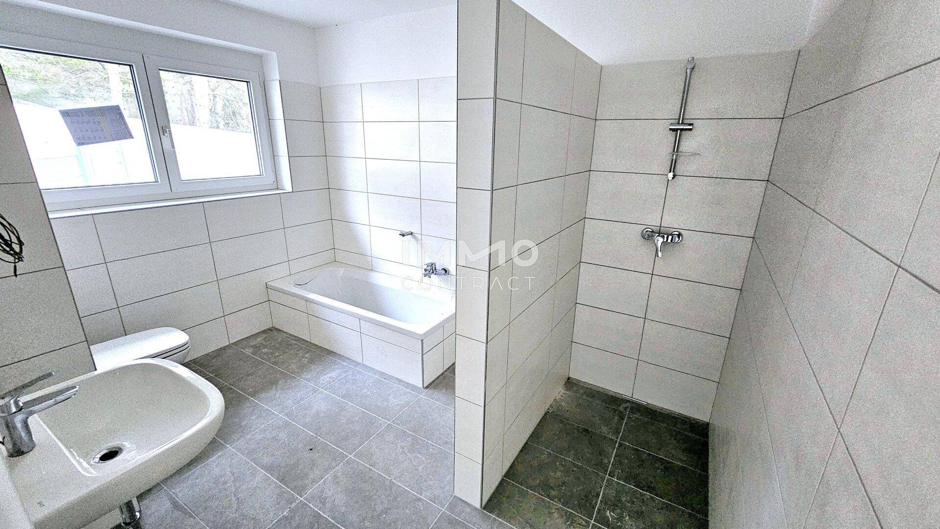 Modernes Badezimmer mit Badewanne, Dusche und Fenster, ausgestattet mit hellen Fliesen.