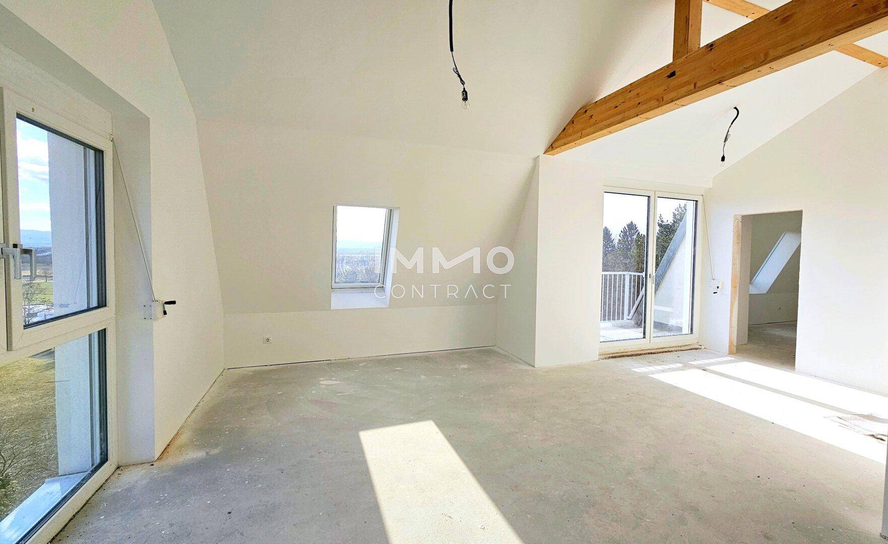 Geräumiger Dachbodenraum mit sichtbaren Holzbalken, großen Fenstern und Zugang zu einem Balkon.