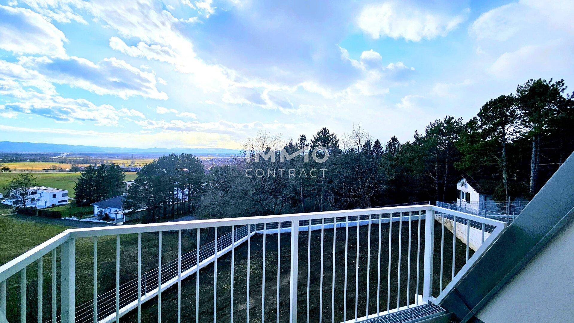Balkon mit weitem Blick über die Landschaft und angrenzende Wälder unter blauem Himmel.