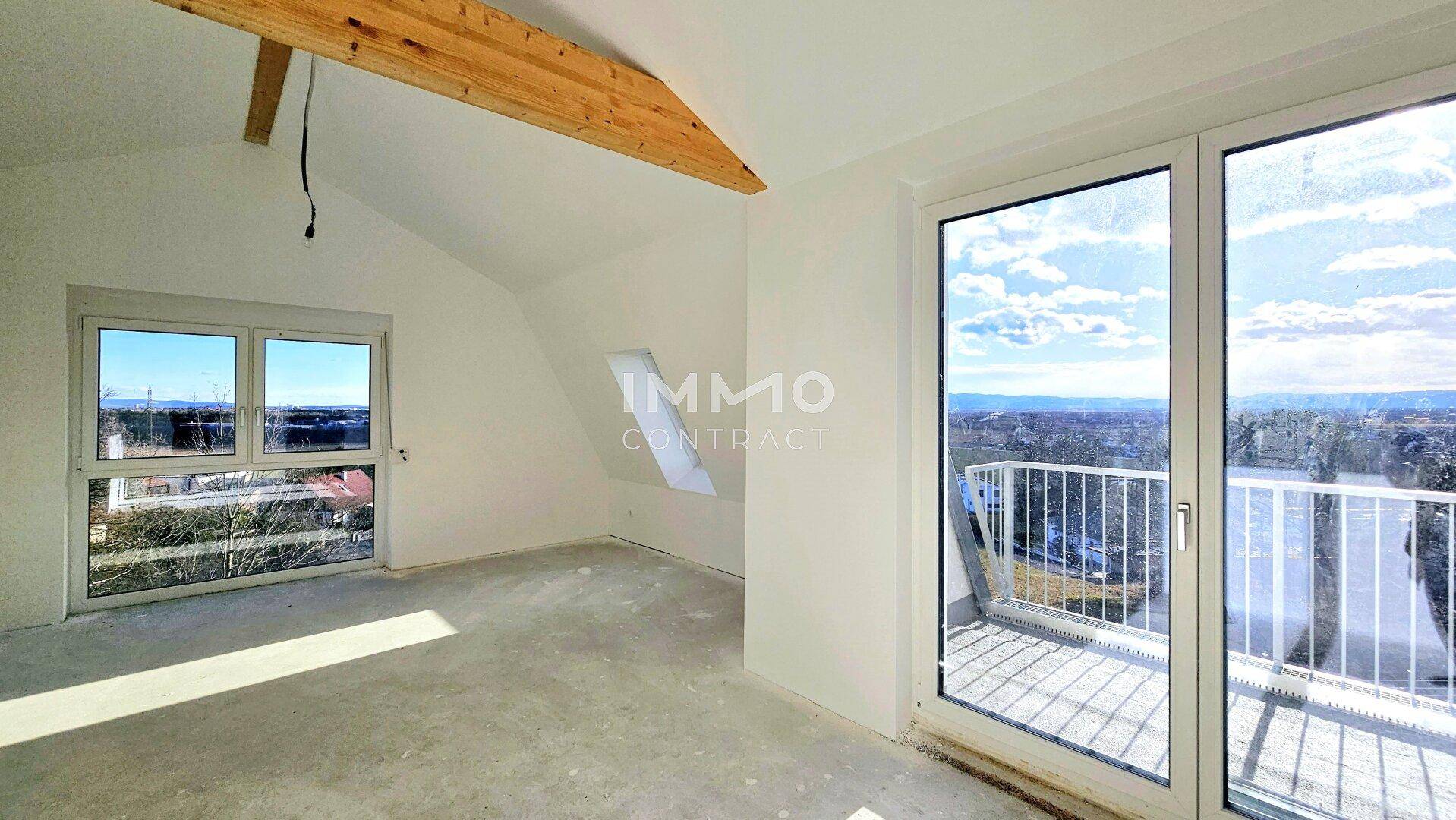 Geräumiger Dachbodenraum mit sichtbaren Holzbalken, großen Fenstern und Zugang zu einem Balkon.