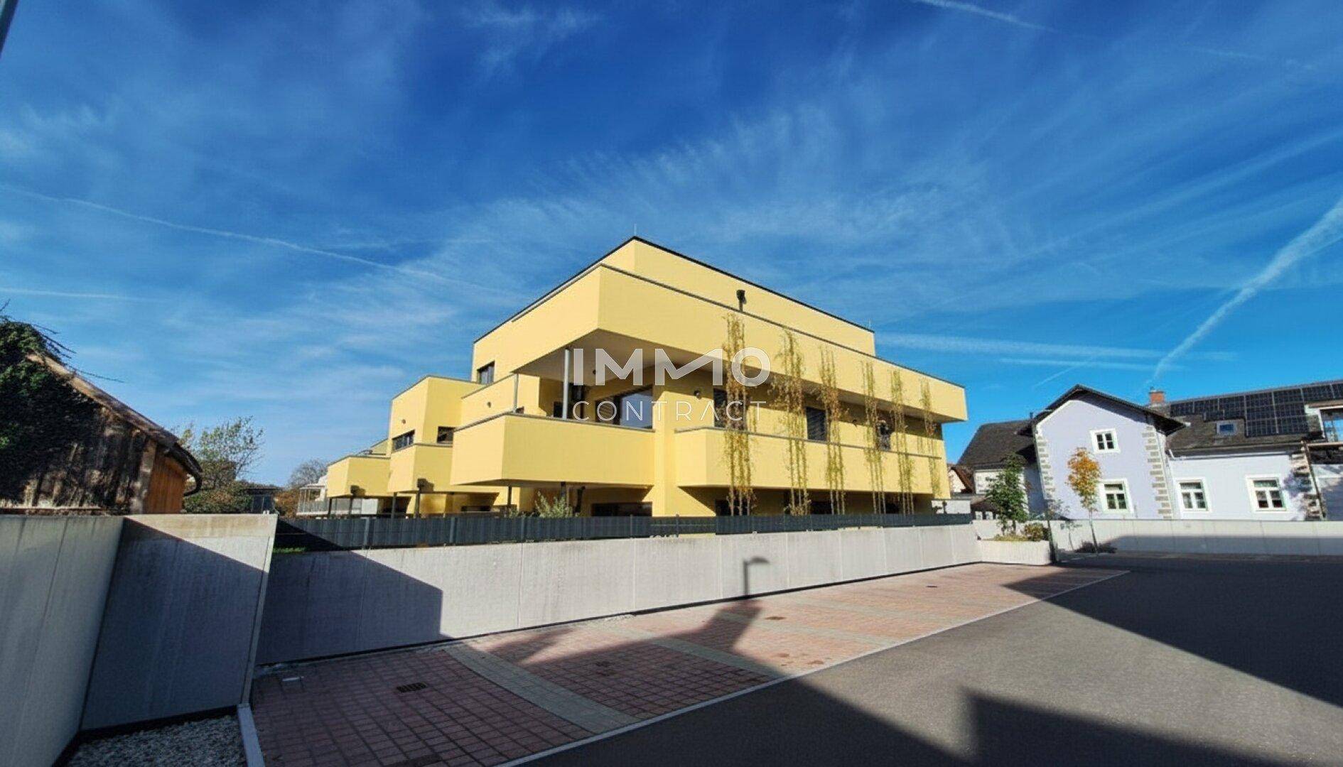 Modernes Mehrfamilienhaus mit gelber Fassade und gestufter Architektur unter blauem Himmel.