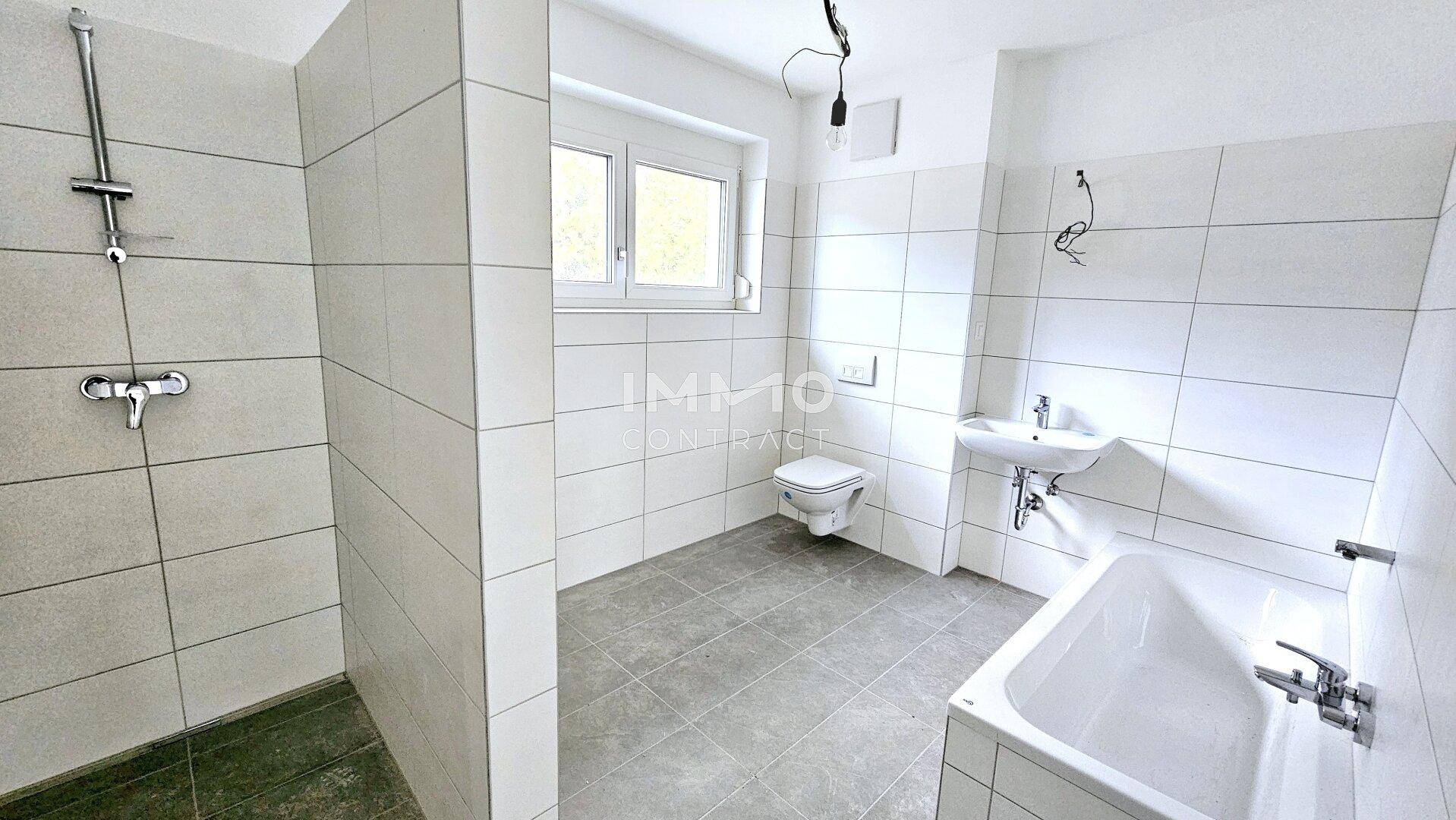 Modernes Badezimmer mit Badewanne, Dusche, WC und Fenster, in hellen Fliesen gehalten.