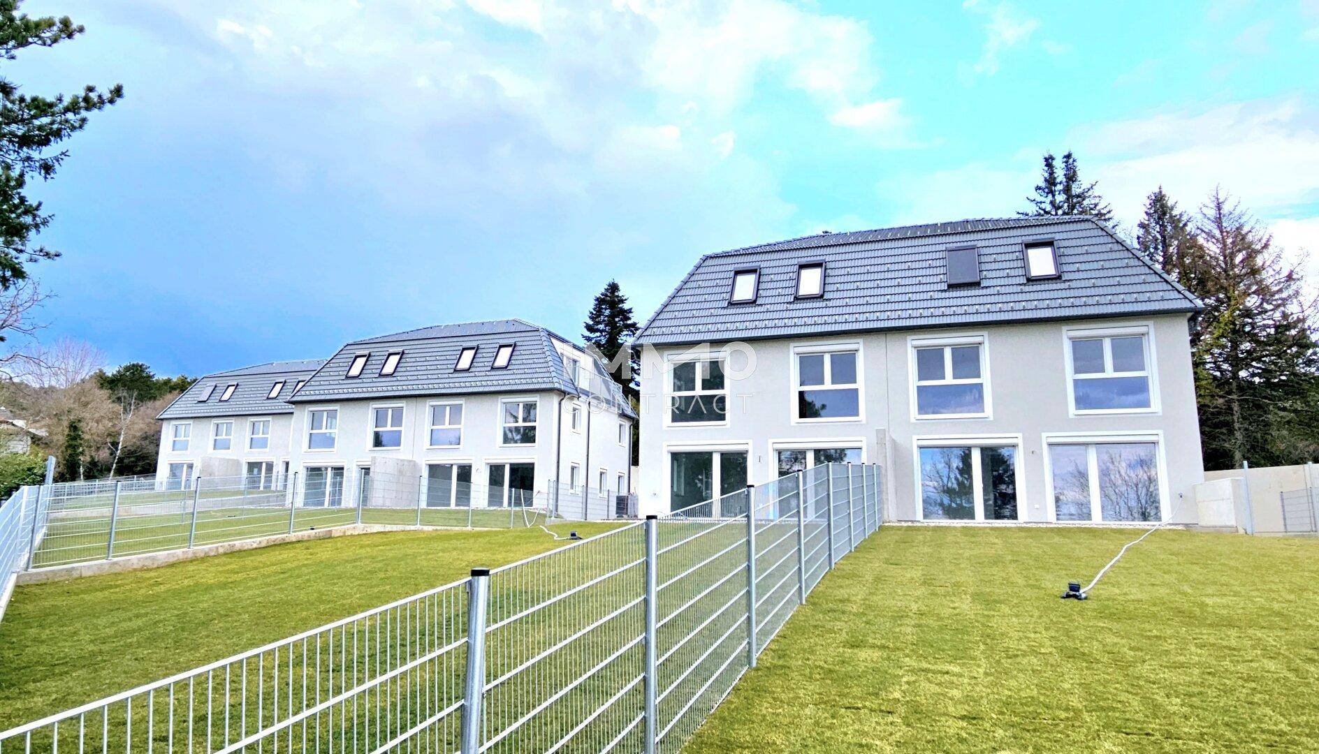 Neubau-Doppelhäuser mit Gärten und Blick auf die grüne Landschaft unter blauem Himmel.