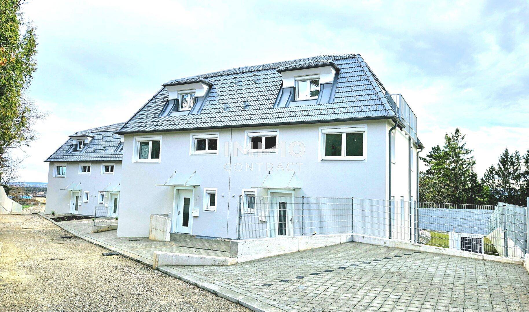 Neubau-Doppelhäuser mit Satteldächern, Parkplätzen und umzäunten Gärten.