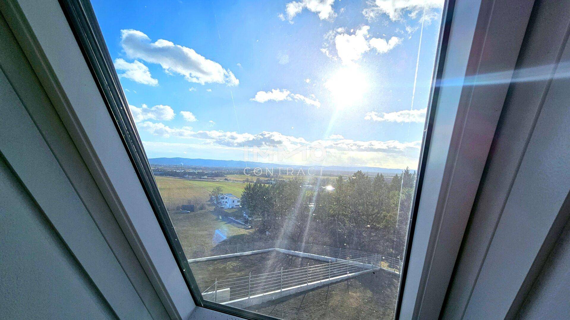 Heller Ausblick durch ein Dachfenster auf die weite Landschaft und den blauen Himmel.