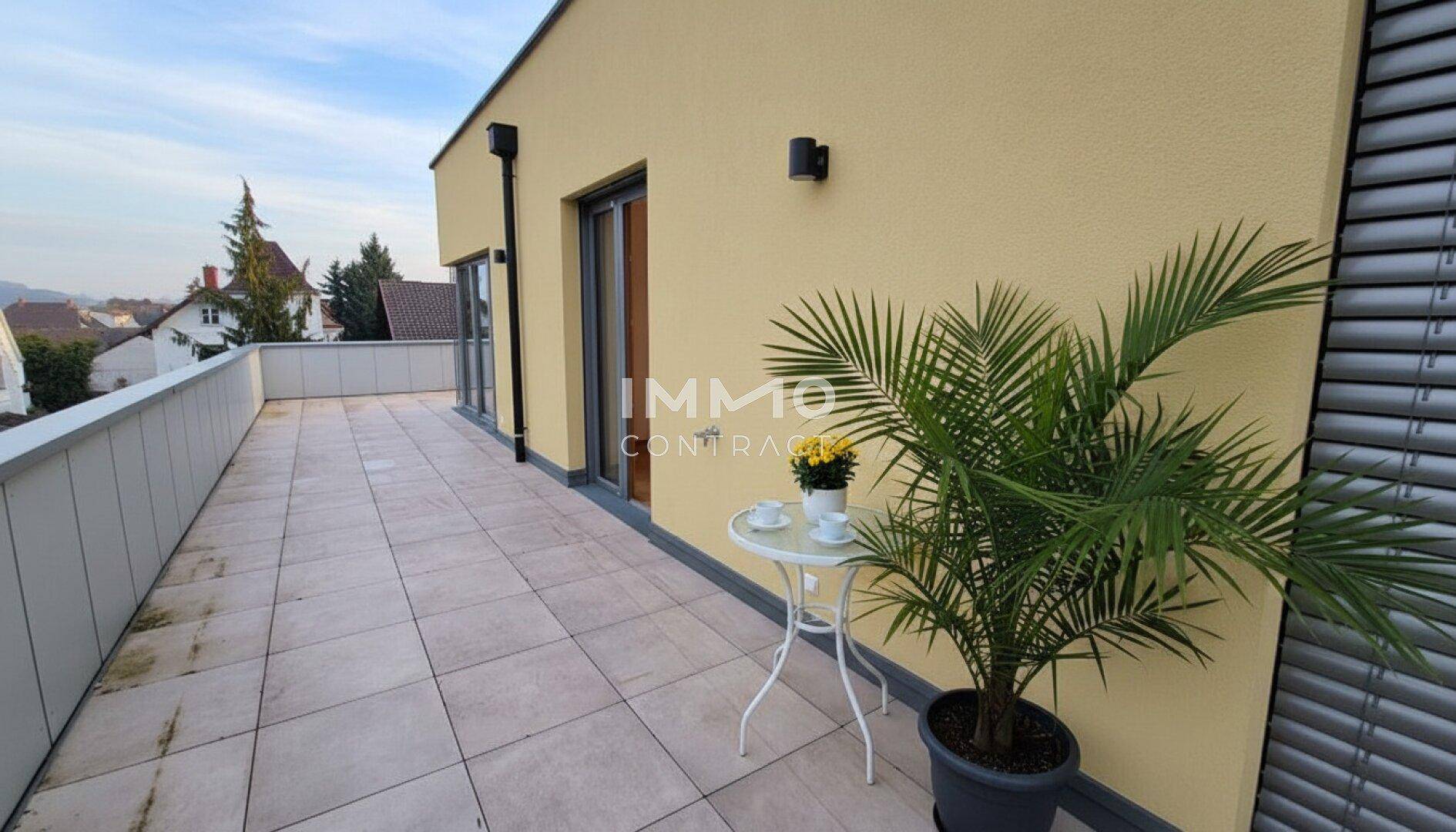 Lange, geflieste Terrasse mit einer Palme und einem kleinen Tisch, ideal für einen Kaffee im Freien.