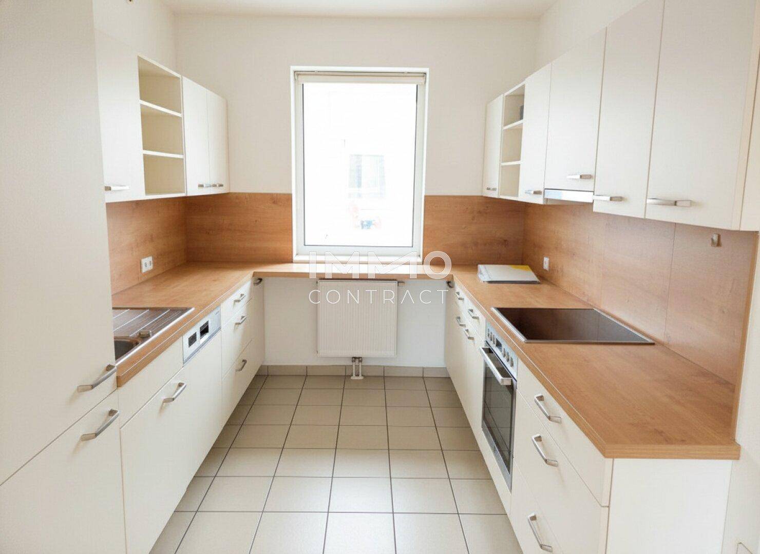 Funktionale Küche mit weißen Schränken, Holzarbeitsplatten, Fliesenboden und Fenster.