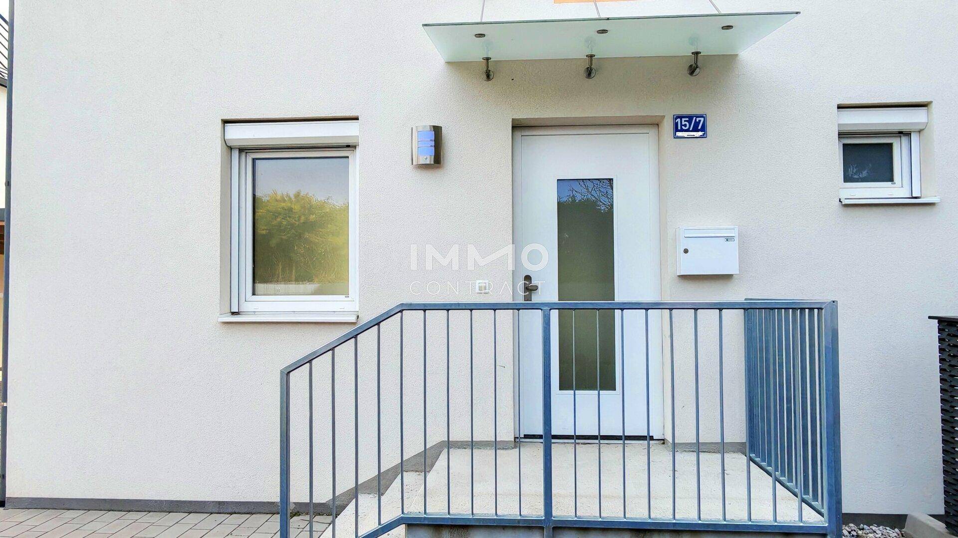 Der Hauseingang mit Vordach, Treppe und Geländer, gut beleuchtet.
