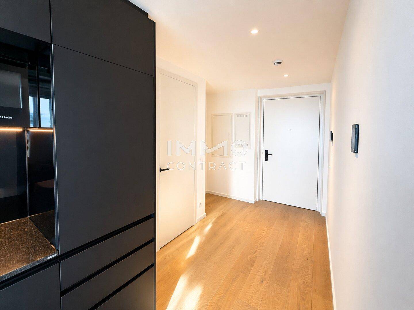 Heller Eingangsbereich mit integrierter Küchenzeile, Holzboden und modernen Türen.