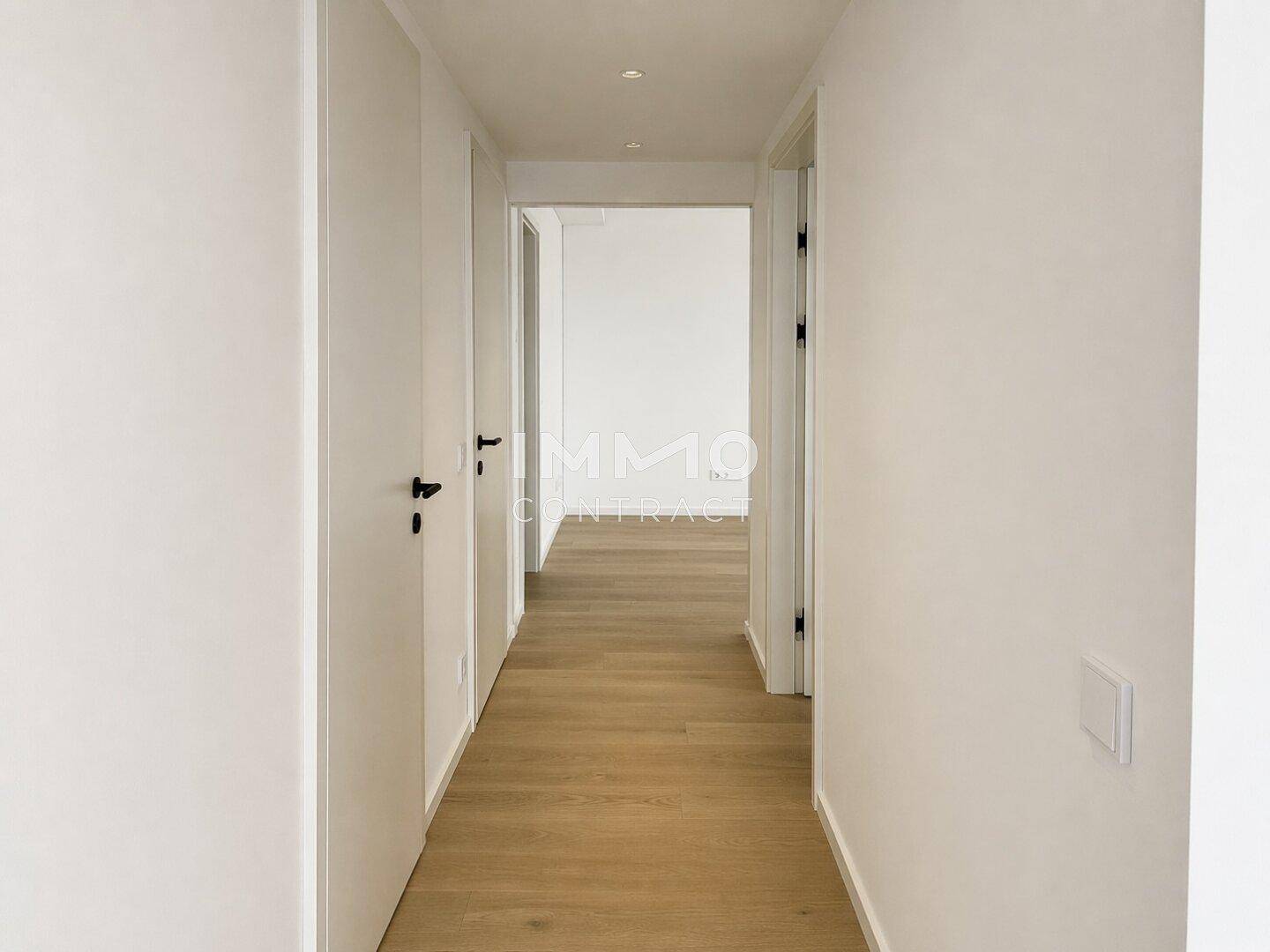 Langer, heller Flur mit Holzboden und weißen Wänden, der verschiedene Zimmer miteinander verbindet.