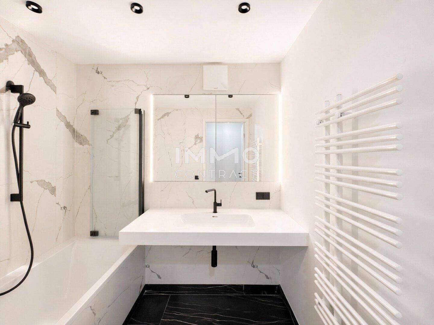 Modernes Badezimmer mit Marmorfliesen, schwarzem Boden, Badewanne und beheiztem Handtuchhalter.