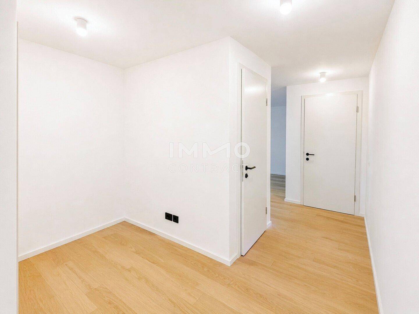Helles Zimmer mit Holzboden und weißen Wänden, das mehrere Türen zu anderen Räumen bietet.