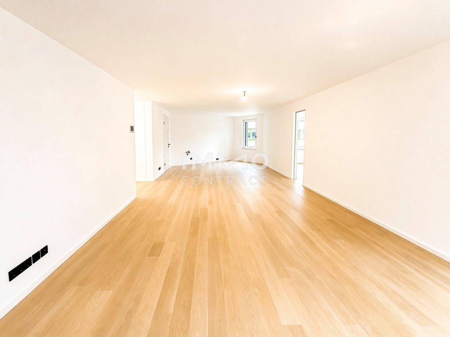 Großer, leerer Raum mit hellem Holzfußboden und viel Tageslicht durch die Fenster.