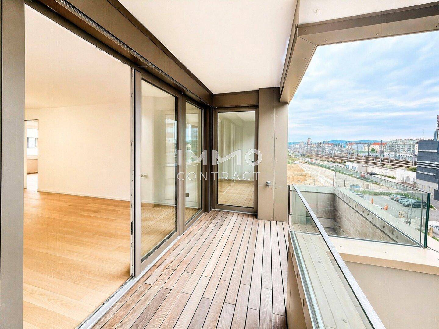 Geräumiger Balkon mit Holzdeck und Glasgeländer, bietet einen weiten Blick auf die Umgebung.