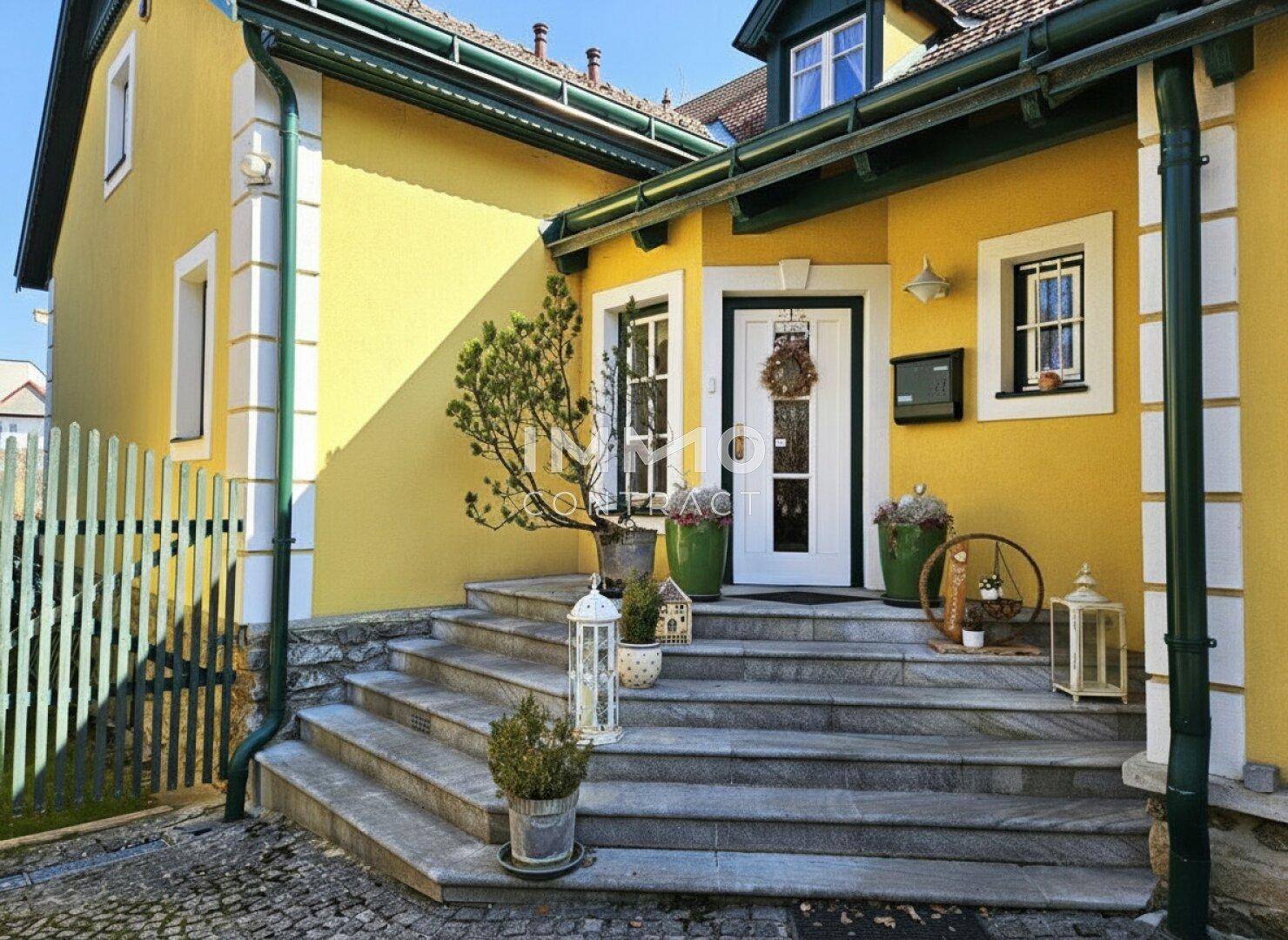 Eingangsbereich eines charmanten Hauses mit gelber Fassade, Steintreppe und grünen Akzenten.