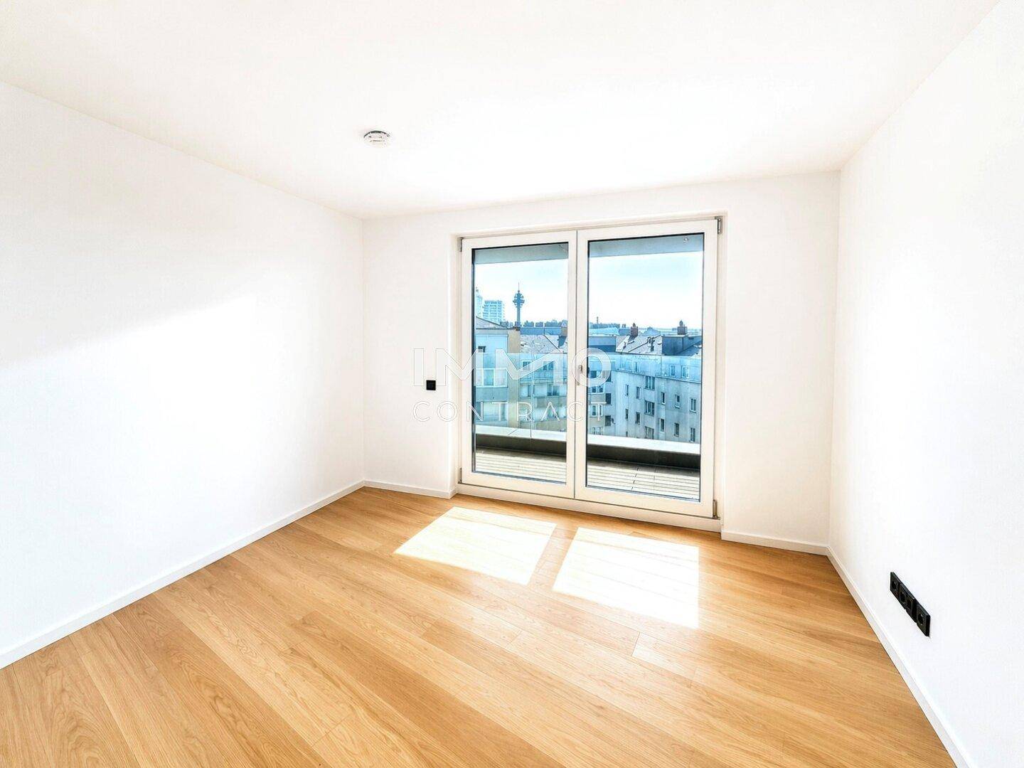 Helles Schlafzimmer mit Parkettboden und großem Fenster mit Blick auf die Stadt.