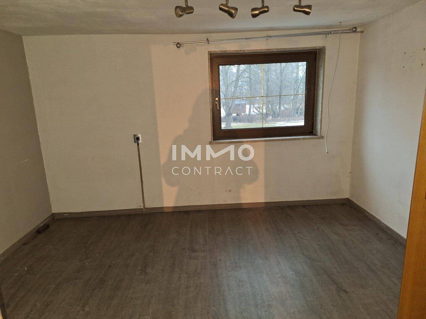 Leerer Raum mit Laminatboden und einem Fenster, das Tageslicht hereinlässt.