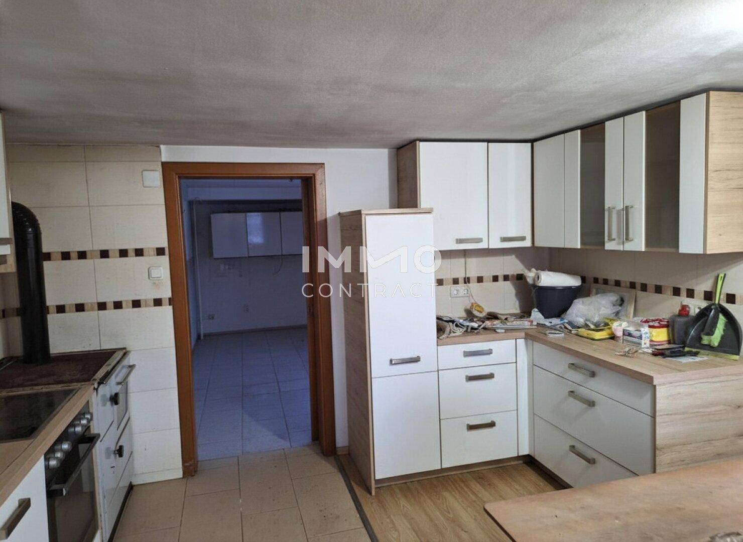 Küche mit Holz- und weißen Schränken, Fliesenboden und Blick in einen weiteren Raum.