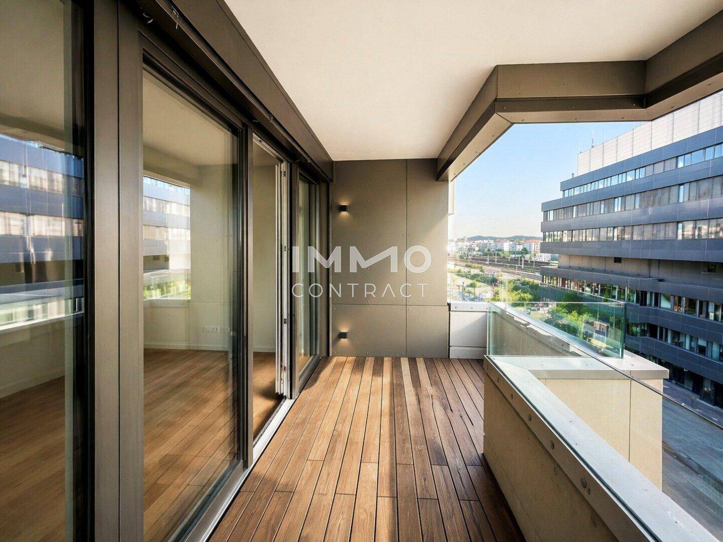 Moderner Balkon mit Holzboden und Glasgeländer, bietet einen weiten Blick auf die Umgebung.
