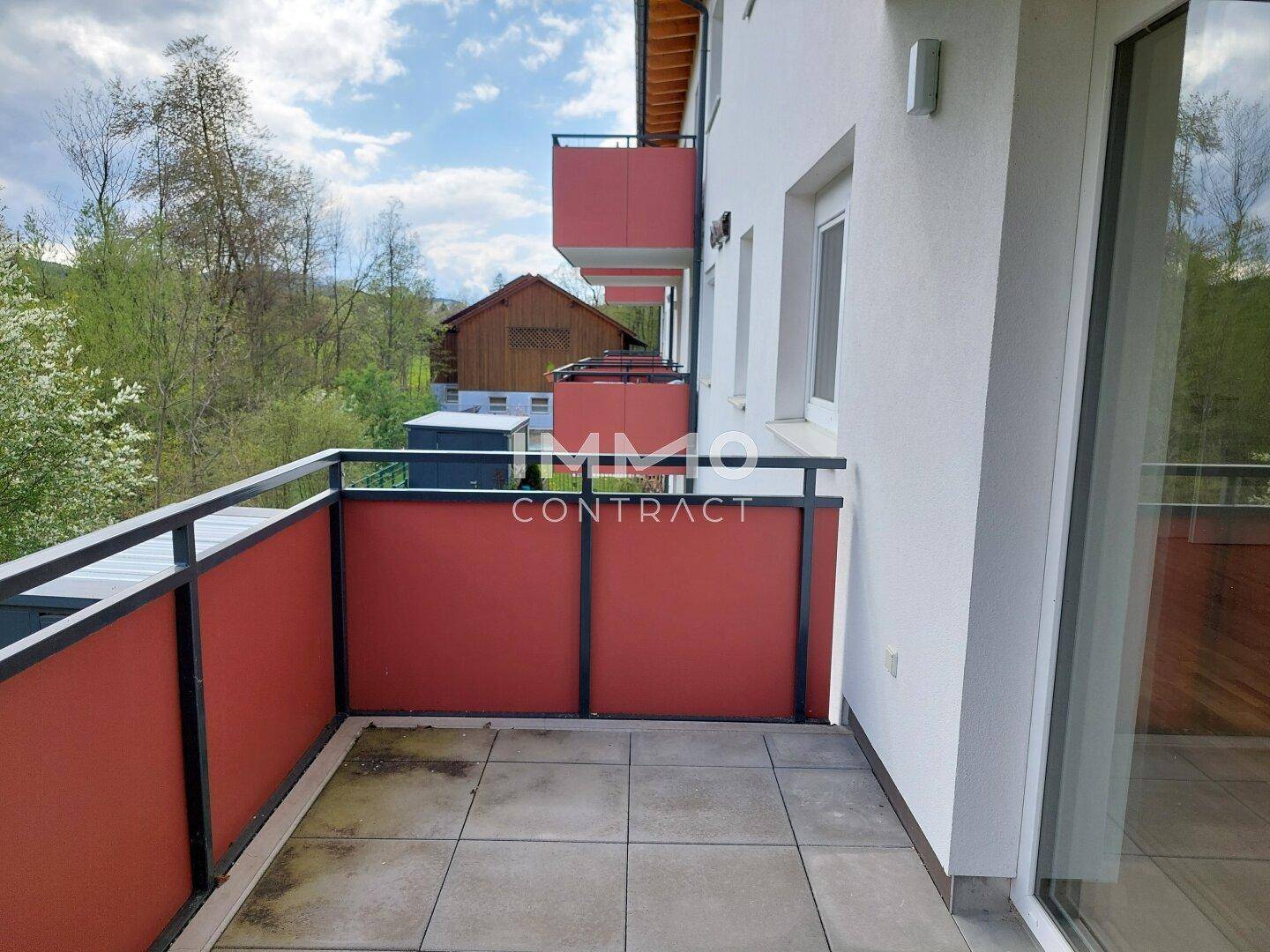 Balkon mit Fliesenboden, roter Brüstung und Blick auf die umliegende grüne Landschaft.