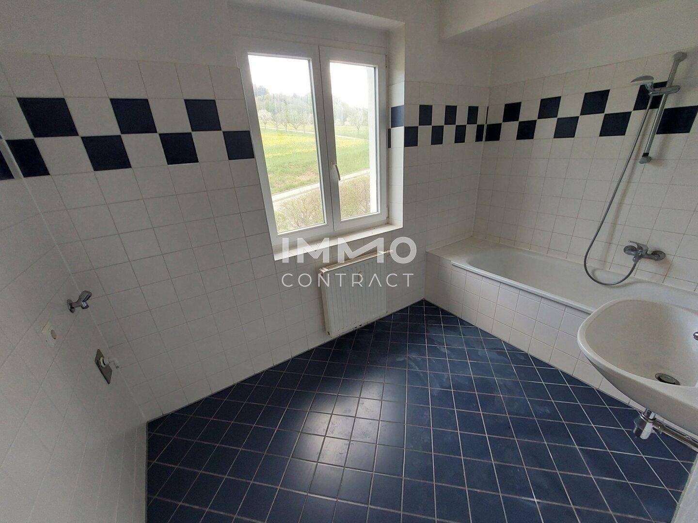 Badezimmer mit Badewanne, Waschbecken und Fenster, gefliest in Weiß und Blau.