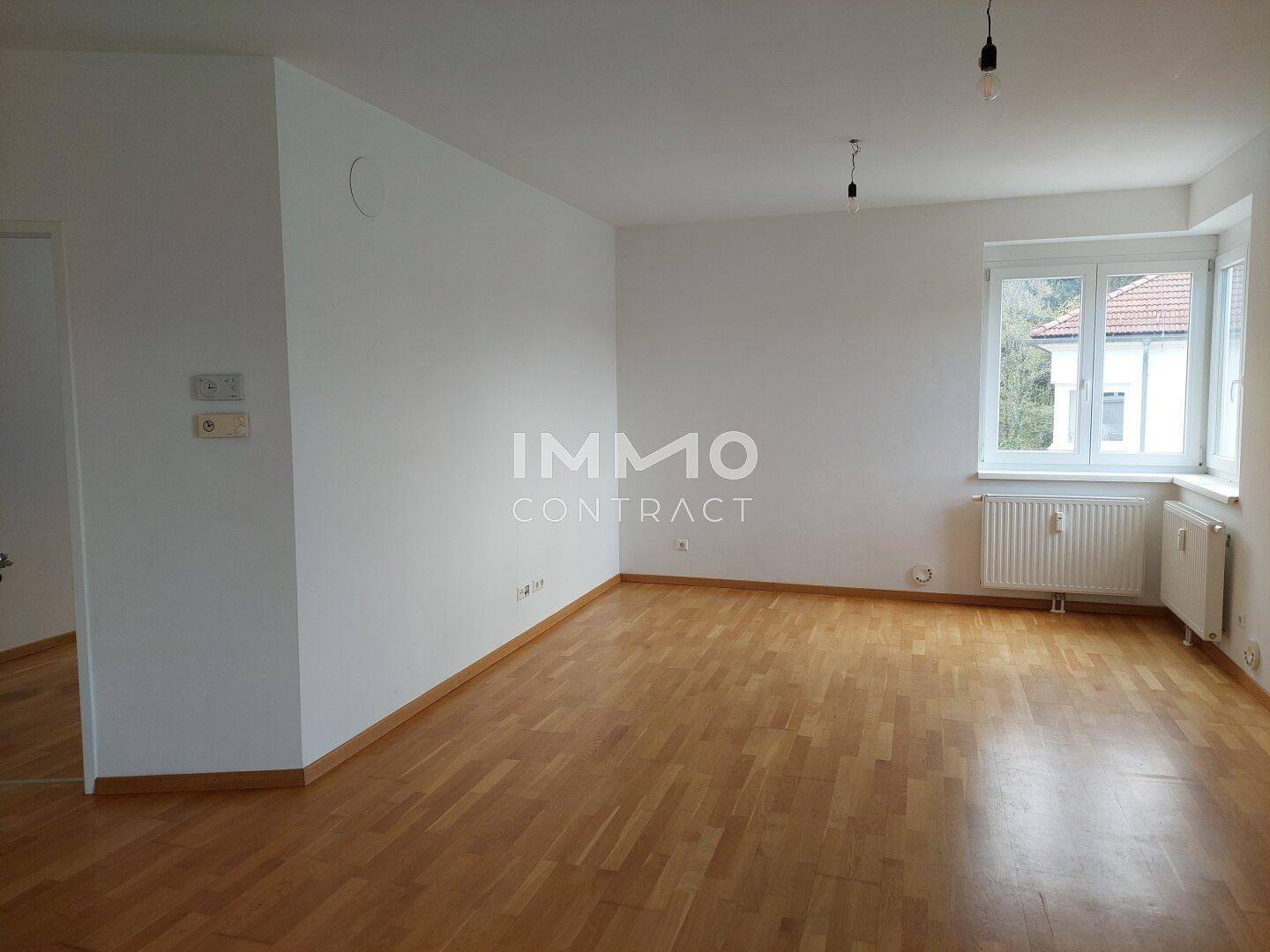 Geräumiges, leeres Wohnzimmer mit hellem Parkettboden und großen Fenstern.