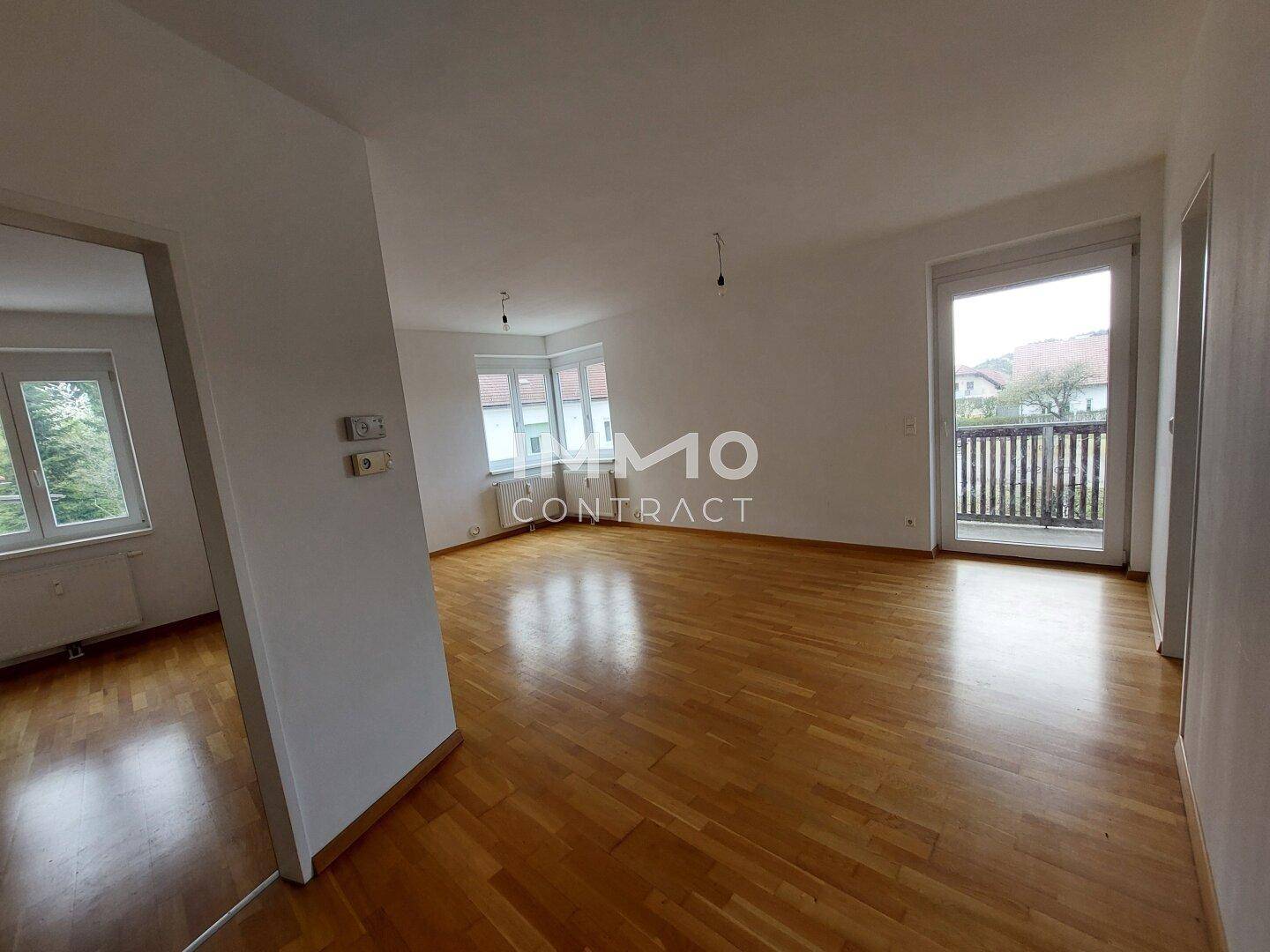 Geräumiger, leerer Wohn-Essbereich mit Parkettboden und Zugang zum Balkon.