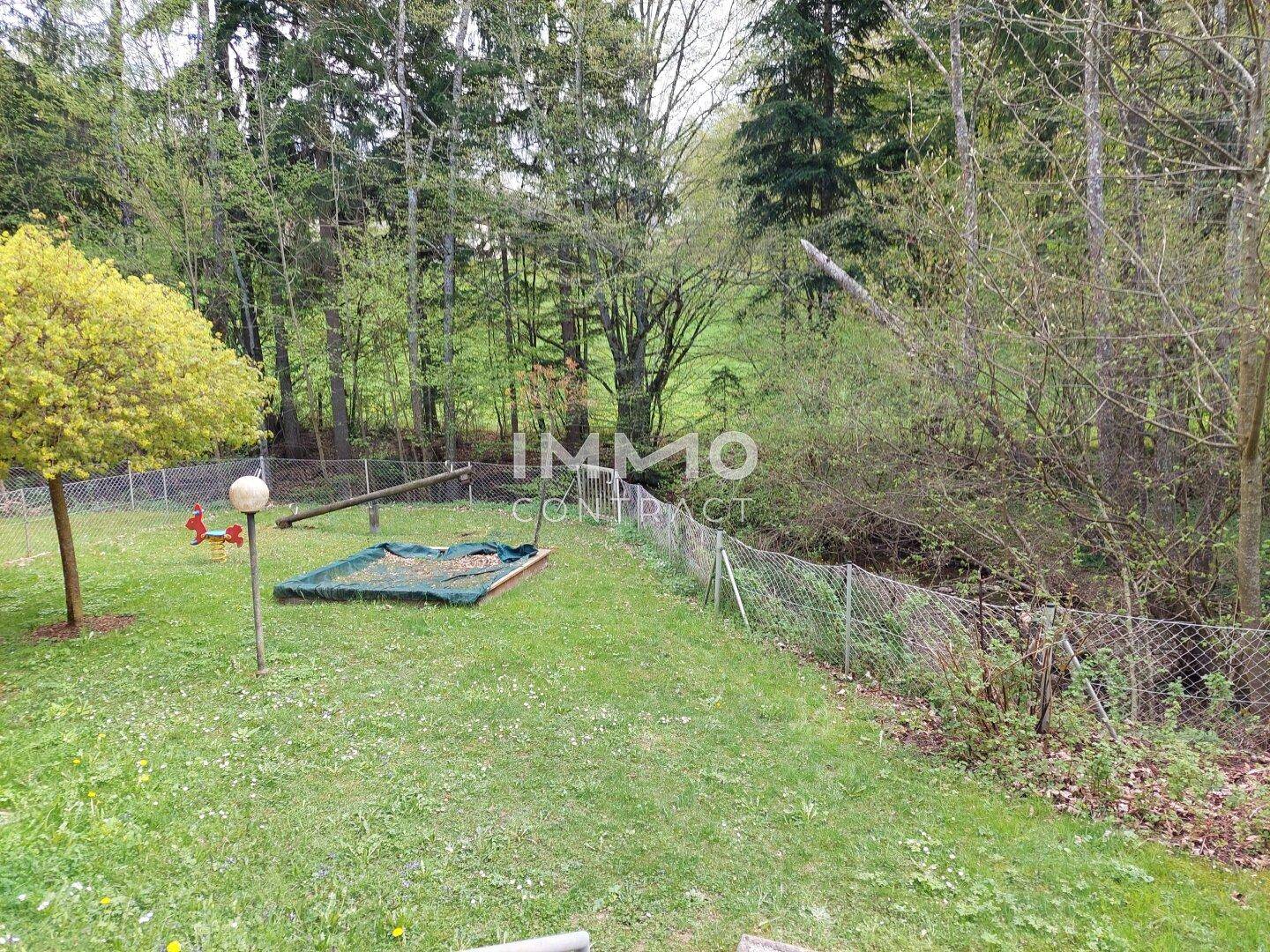 Grüner Gartenbereich mit Sandkasten und Spielgeräten, umgeben von Bäumen.