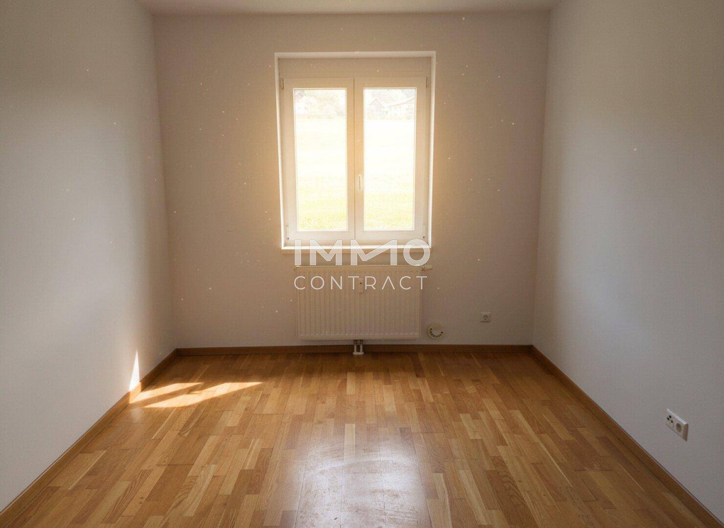 Heller, leerer Raum mit Parkettboden und großem Fenster, ideal für Schlafzimmer oder Büro.