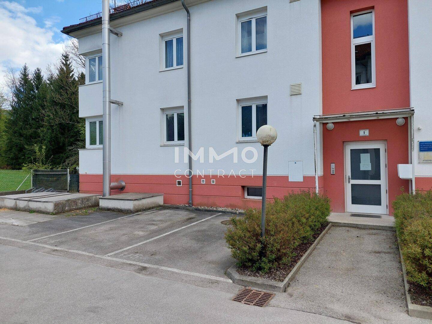 Vorderansicht des Mehrfamilienhauses mit Eingangsbereich und Parkplätzen.
