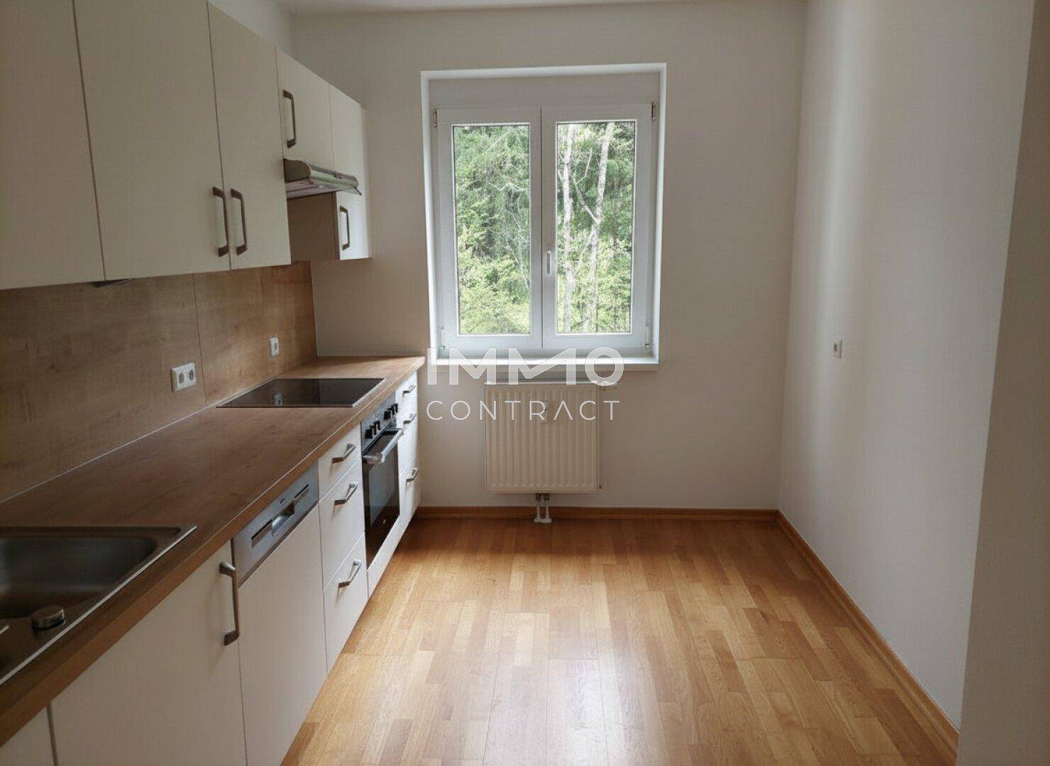 Funktionale Küche mit weißen Schränken, Holzoptik-Arbeitsplatte und Fenster mit Blick auf Bäume.