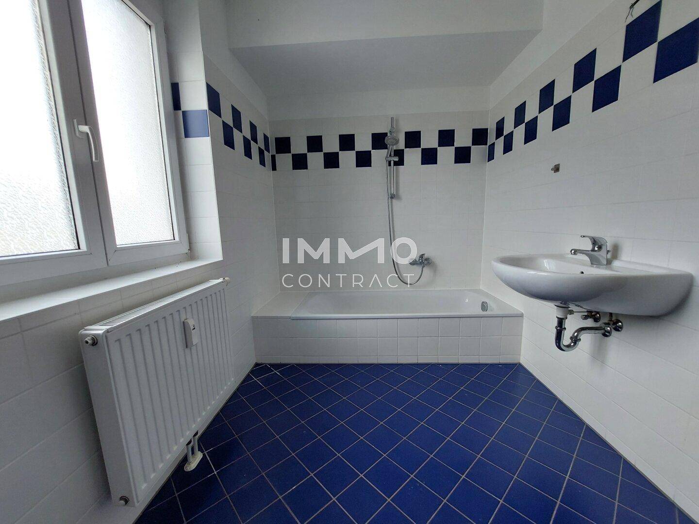 Badezimmer mit blauen Fliesen, Badewanne und Fenster für natürliche Belüftung.