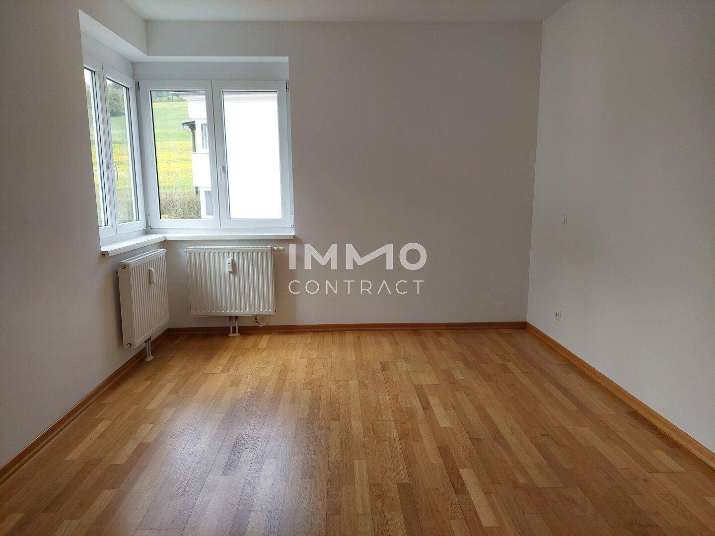 Helles Schlafzimmer mit Parkettboden und großen Fenstern, die viel Tageslicht hereinlassen.