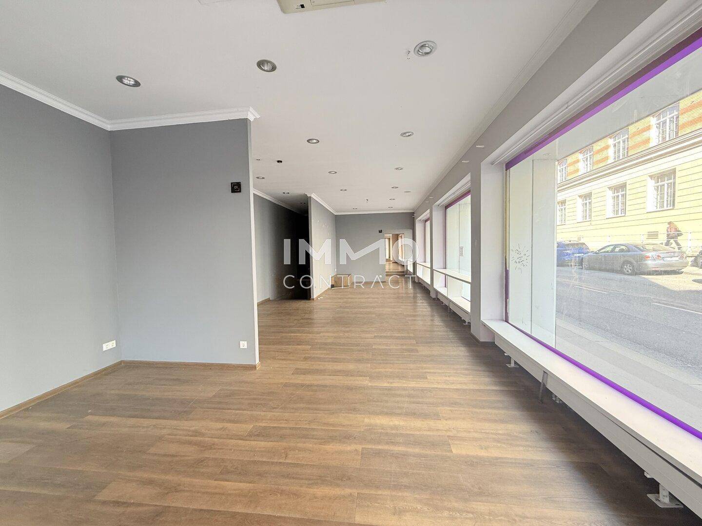 Langer, offener Geschäftsraum mit großen Schaufenstern zur Straße und modernem Laminatboden.