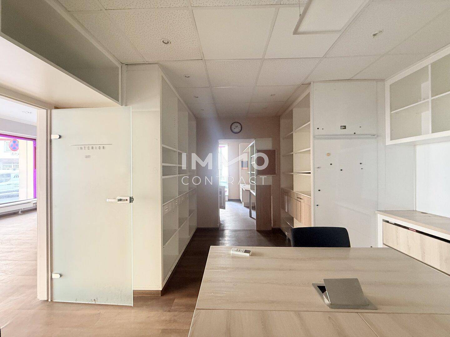 Flurartiger Bürobereich mit vielen Einbauschränken und einem Schreibtisch, der zu weiteren Räumen führt.
