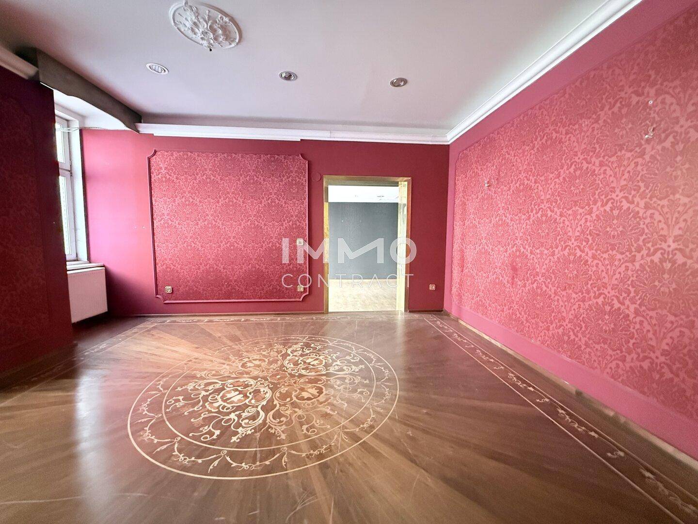 Eleganter Raum mit roter Tapete und kunstvollem Parkettboden, der eine luxuriöse Atmosphäre schafft.