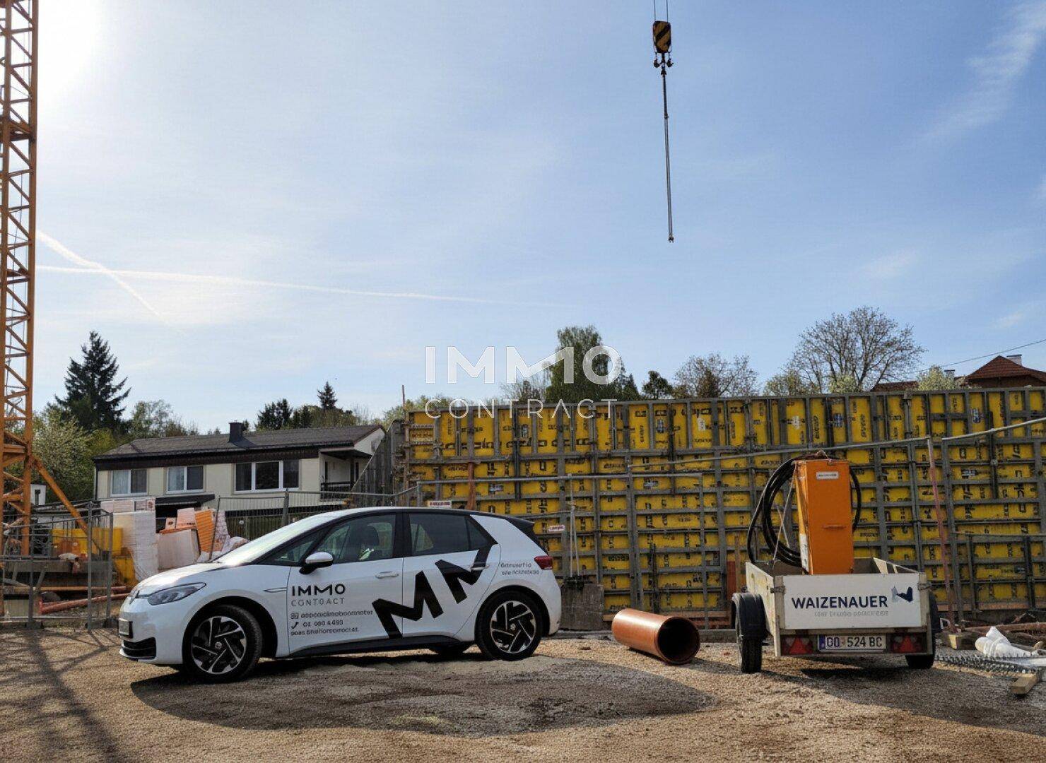 Baustelle mit Schalung für eine Betonwand, Baufahrzeug und Kran unter strahlend blauem Himmel.
