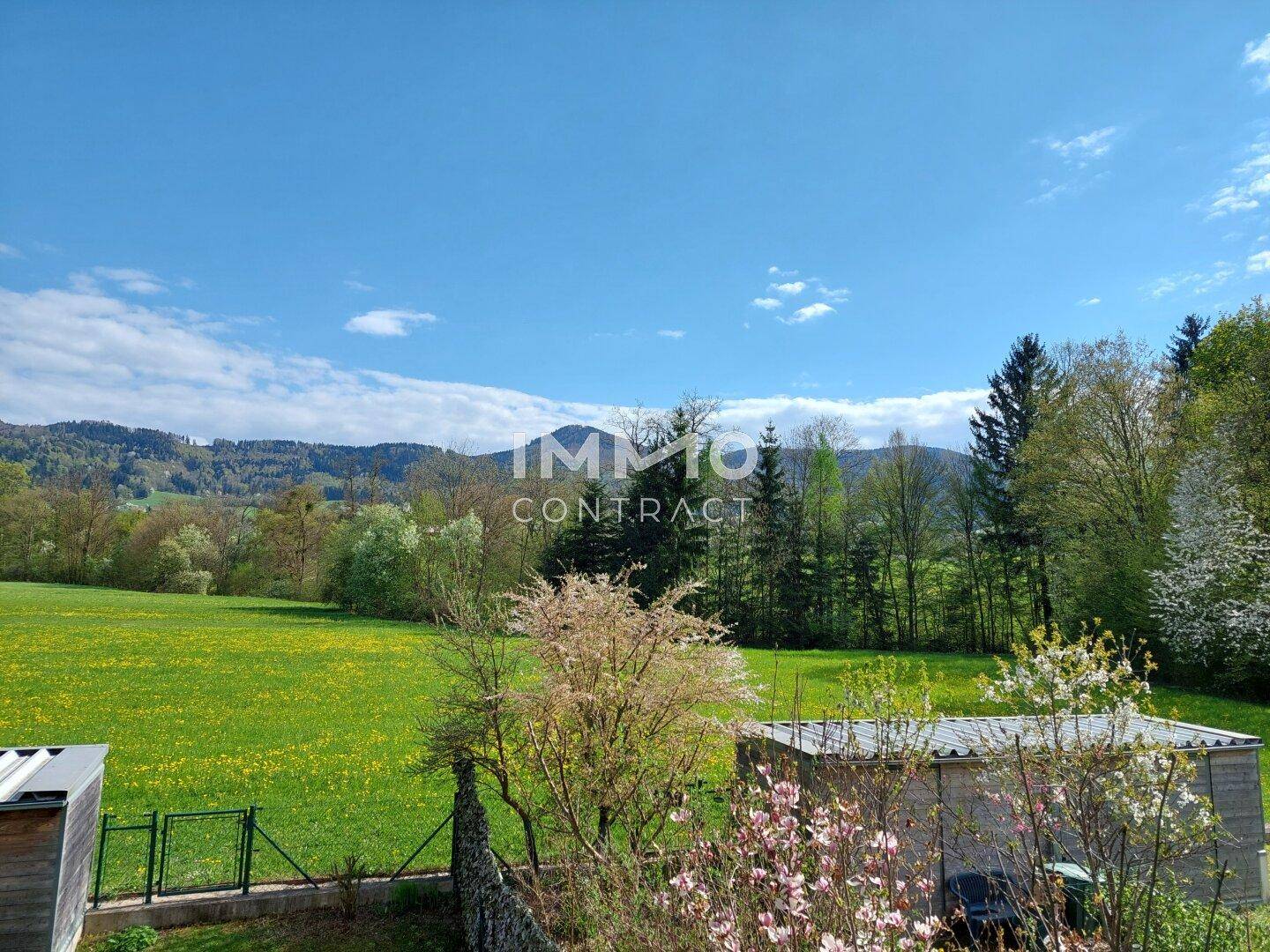 Weitläufiger Blick über grüne Wiesen und bewaldete Hügel unter blauem Himmel.