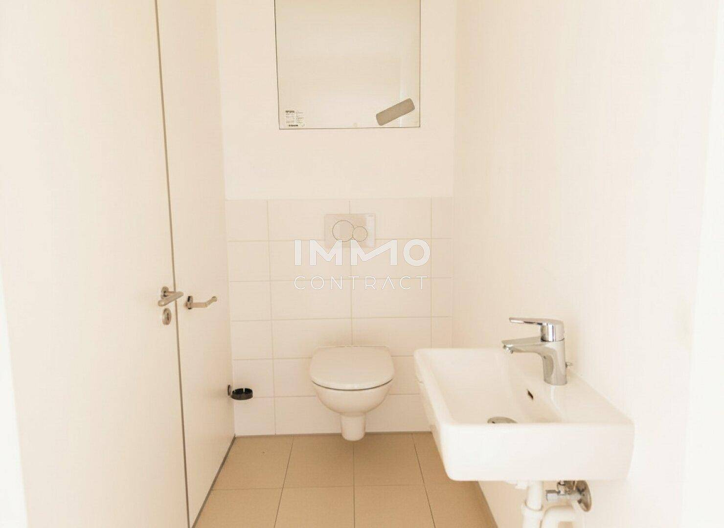 Kleines Gäste-WC mit Wand-WC, Waschbecken und hellen Fliesen.